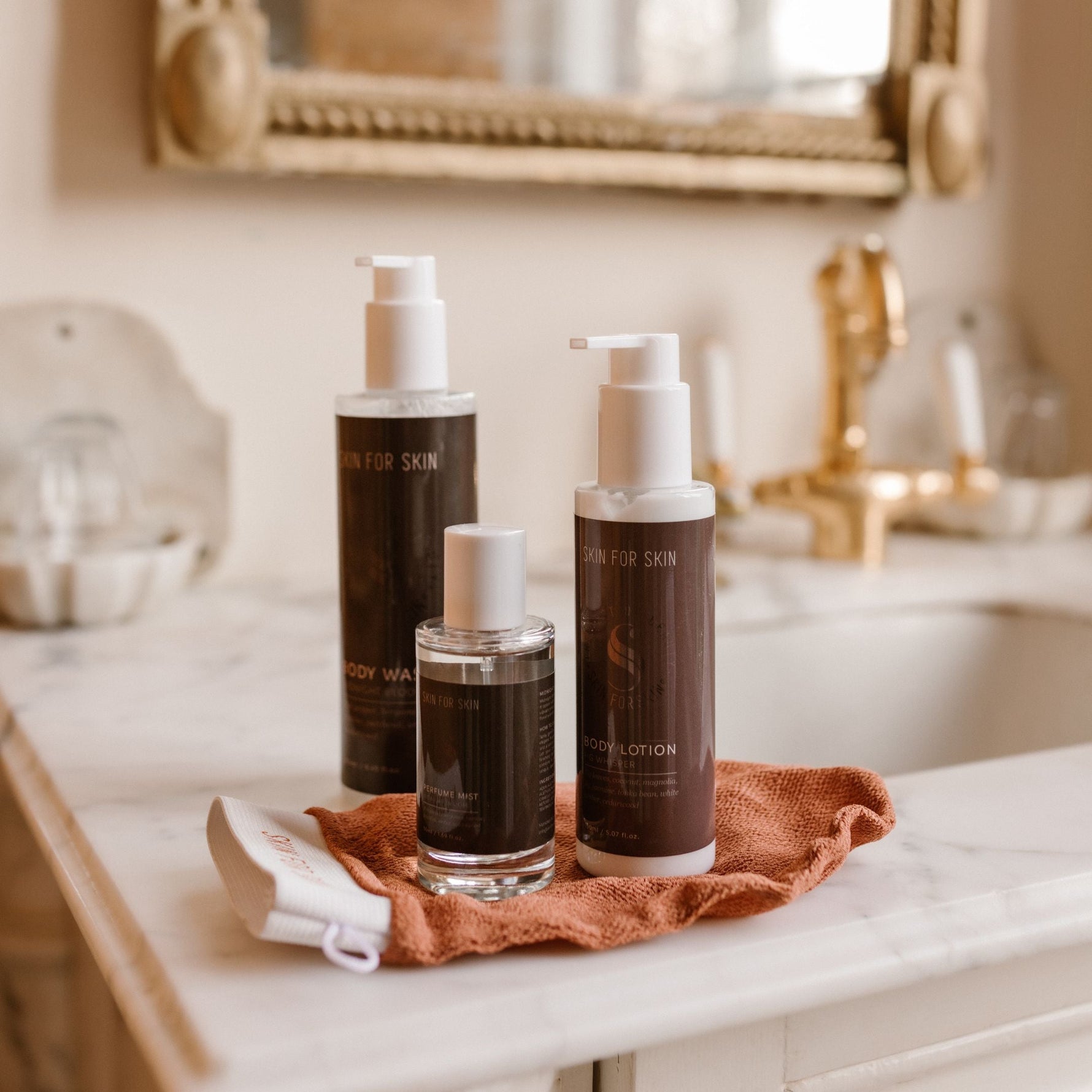 drie flesjes met bodywash producten staande op een scrubhandschoen op de rand van een wastafel