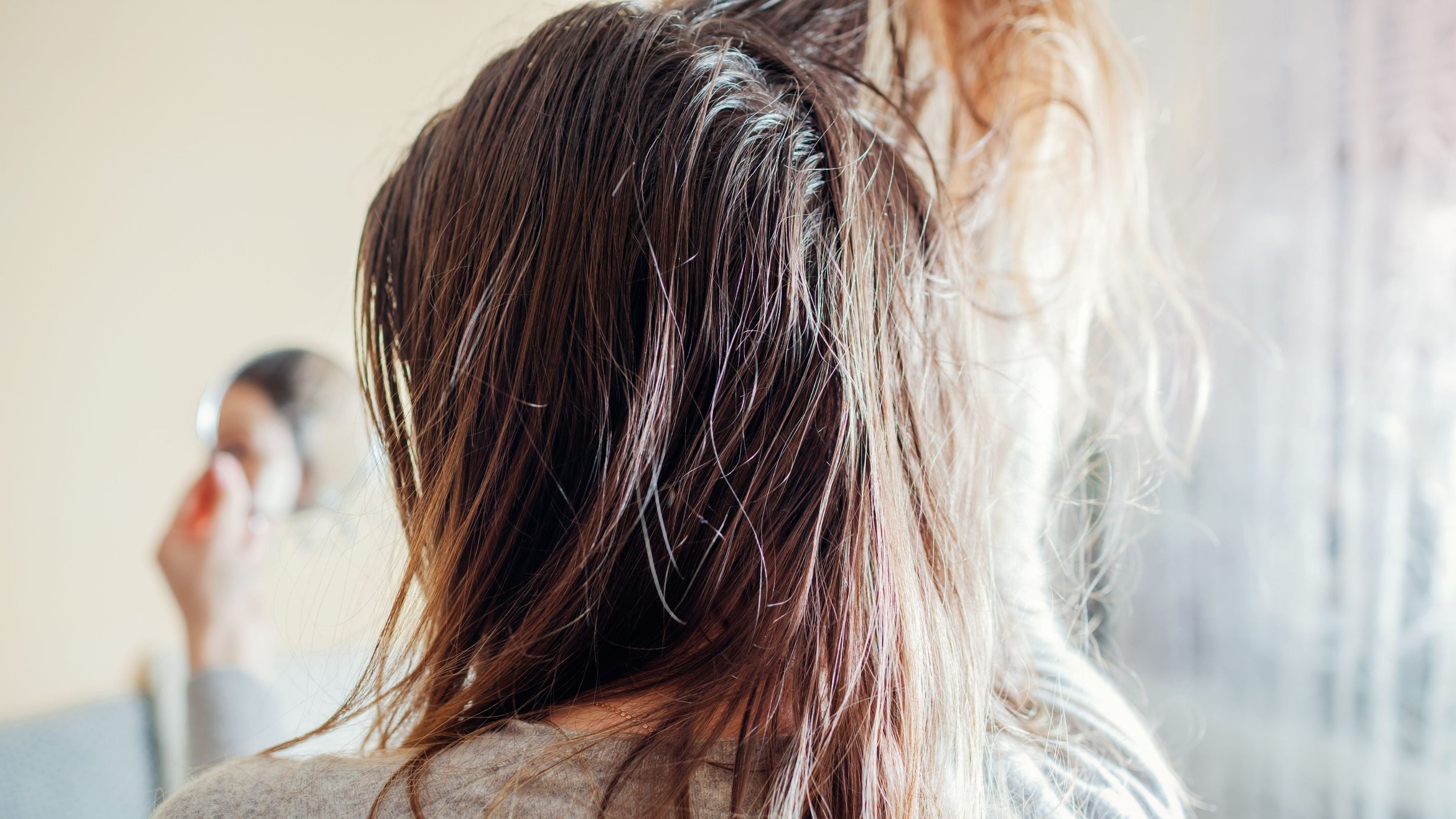 Persoon met lang haar gezien van achteren voor een spiegel