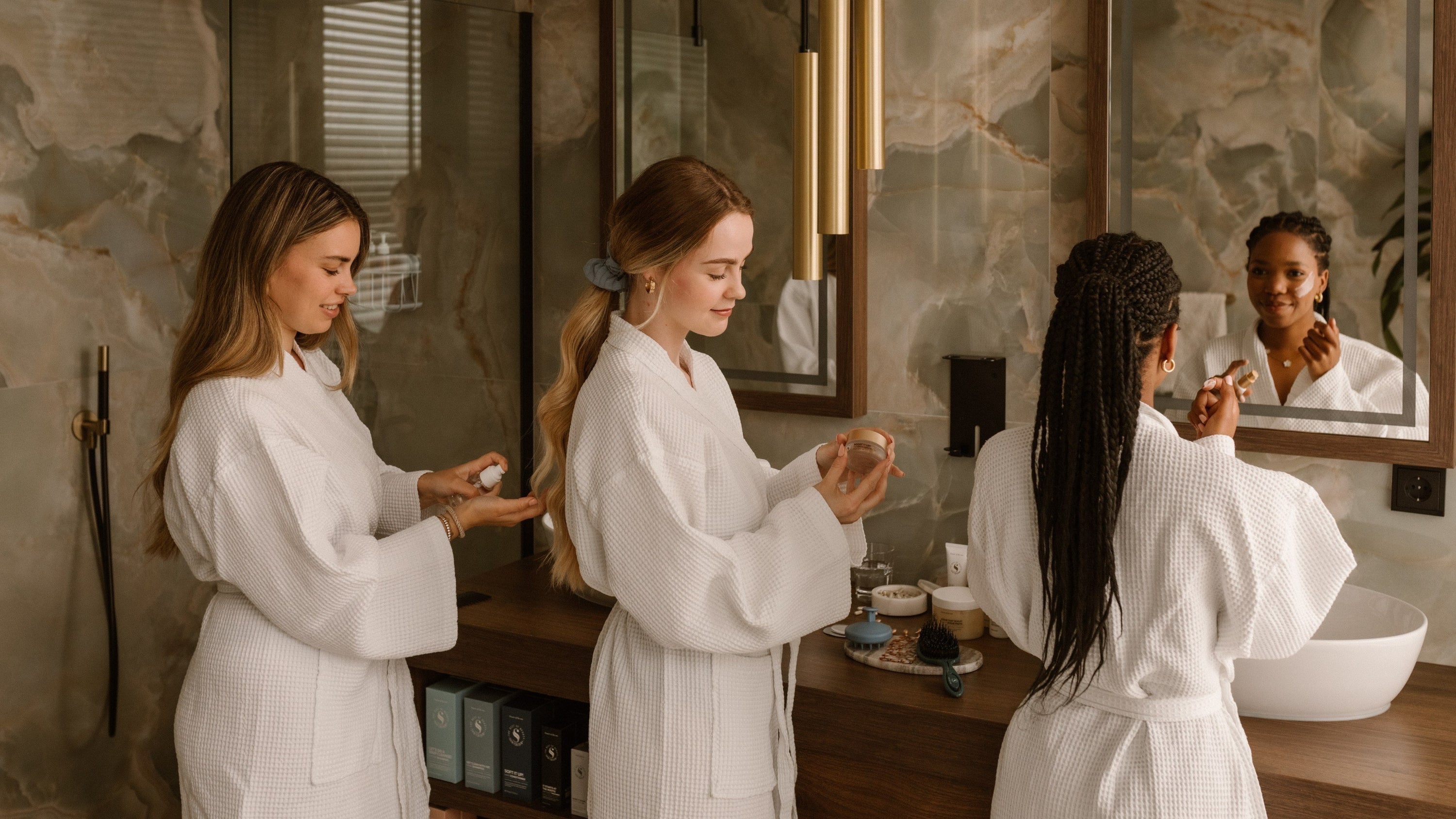 drie vouwen in een badjas voor de spiegel bezig met een beauty routine