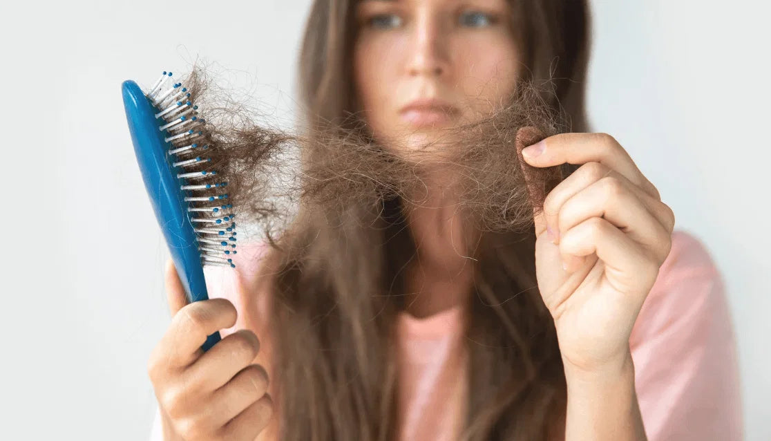 afbeelding van een vrouw die teleurgesteld kijkt naar haar haarborstel vol met haar in de herfstperiode