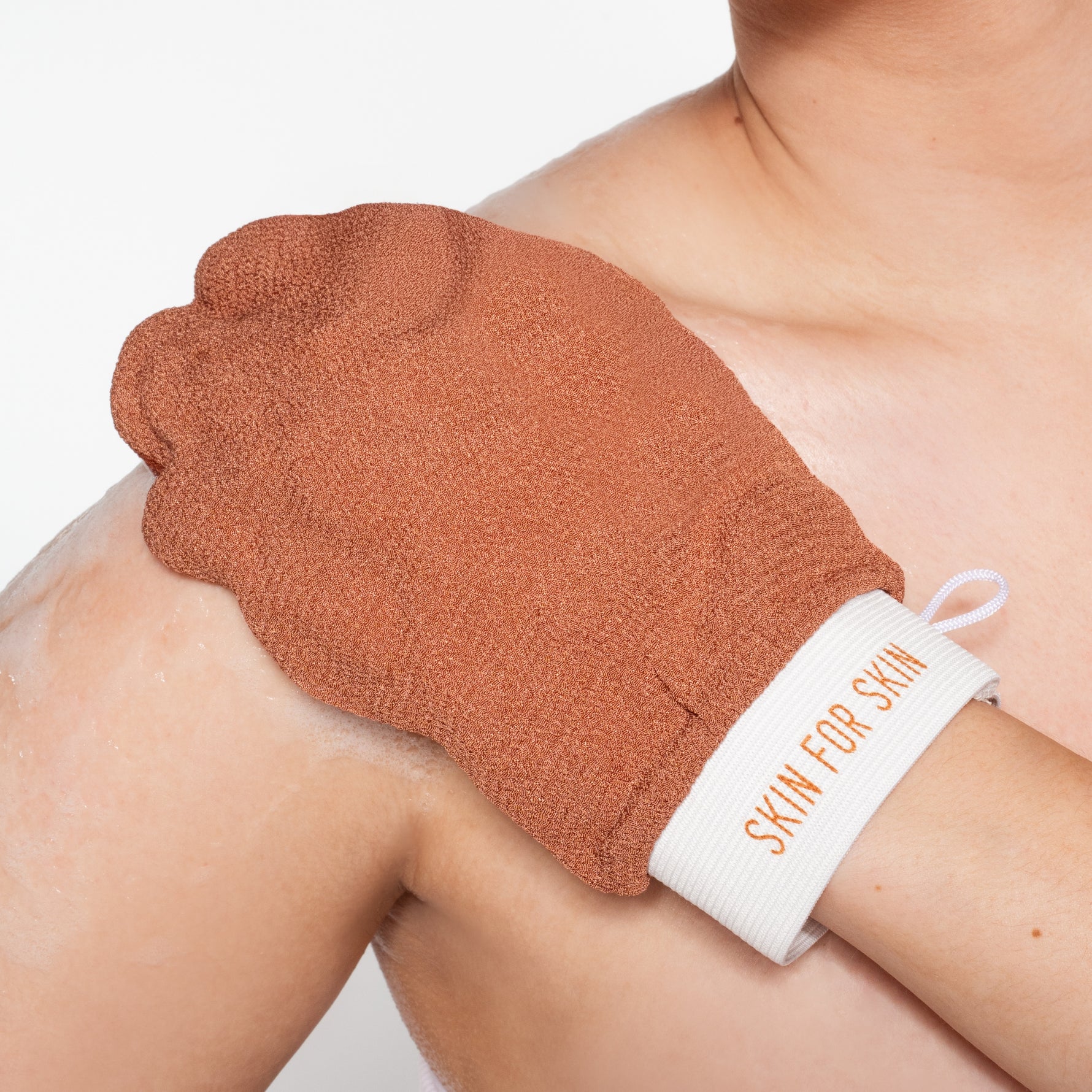Hand met Skin for Skin scrubhandschoen reinigt de huid voor een zachte, gladde finish.