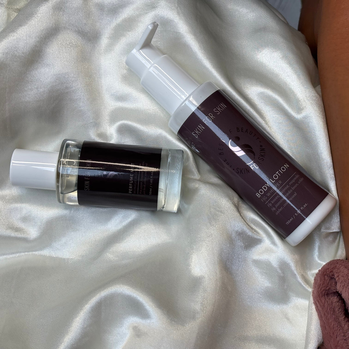 Lichaamsverzorging producten van Skin for Skin met body lotion en perfume mist op een zachte satijnen achtergrond.