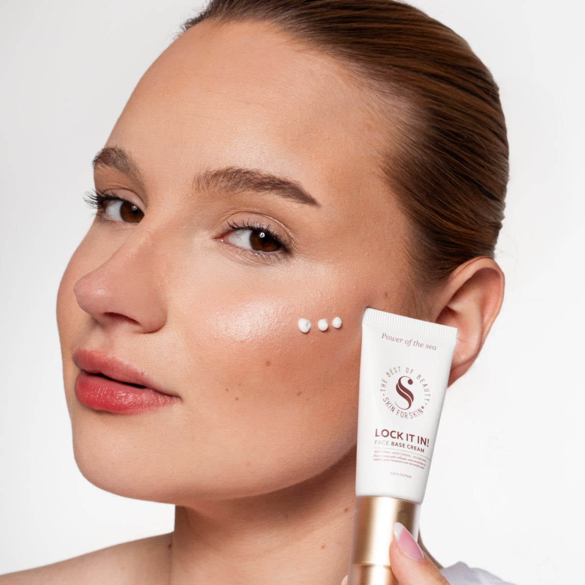 Vrouw toont Skin for Skin Lock It In face base cream met stipjes crème op haar wang.