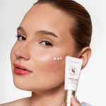 Vrouw toont Skin for Skin Lock It In face base cream met stipjes crème op haar wang.
