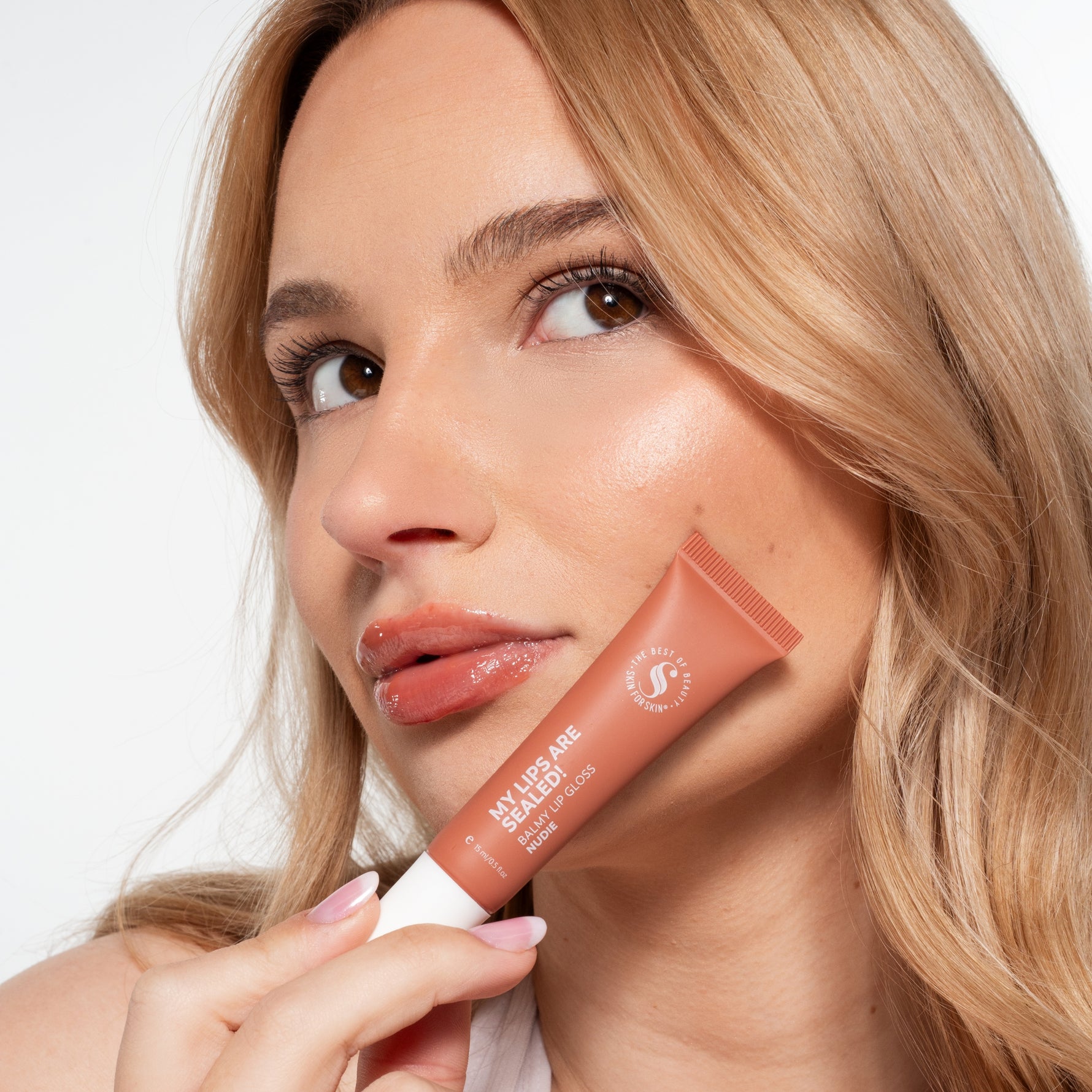 Vrouw toont Skin for Skin My Lips Are Sealed balmy lip gloss in Nude voor een glanzende, verzorgde look.